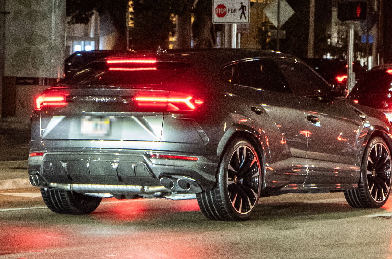 Traseira de um Lamborghini Urus cinza à noite, com as lanternas vermelhas acesas e a tampa do porta-malas fechada